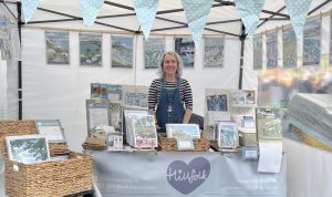 South Devon artist Beth Hill, owner of Hillfolk illustration, standing behind a display of her artwork featruing local views