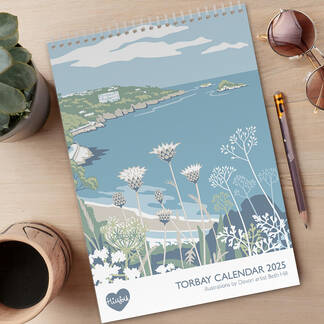 overhead view of a desk with the Hillfolk Torbay Calendar cover, featuring view of meadfoot beach