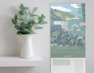hillfolk calendar on wall next to shelf with plant. Calendar features view of Oddicombe for the month of August
