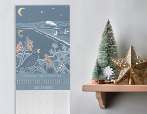 hillfolk calendar on wall next to shelf with plant. Calendar features view of Goodrington for the month of Deceomber